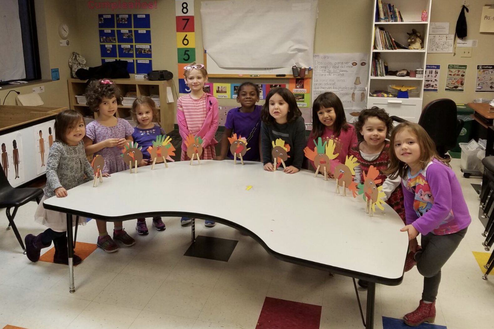 Pre-K students standing behind a table of paper turkeys they made