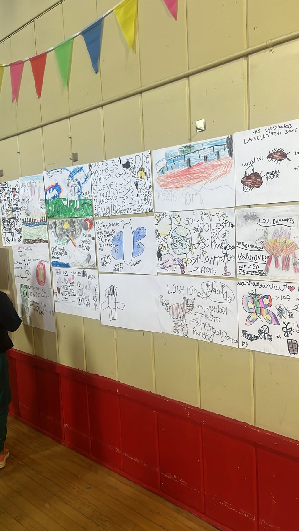 A hallway wall covered in student writing and drawings in Spanish