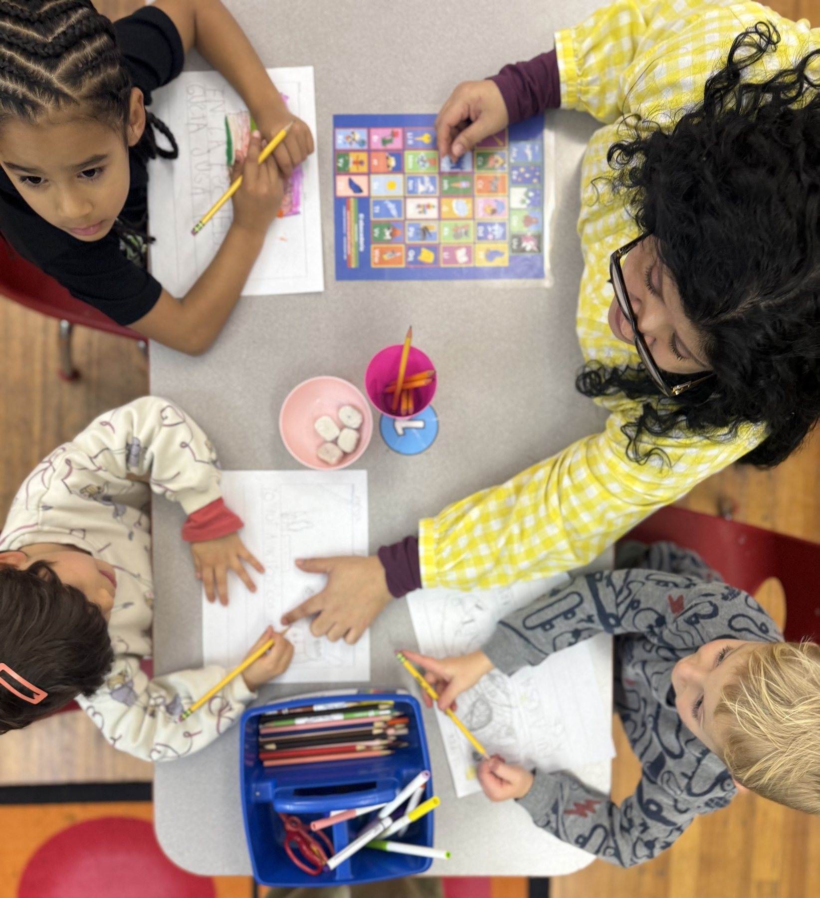An Amistad teacher writing alongside four students at a classroom table
